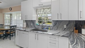 A modern kitchen with white cabinets, a granite countertop, and a window with a leaf-patterned curtain.