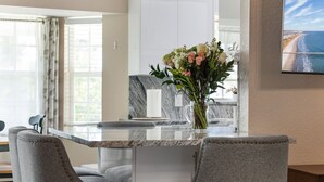 A modern kitchen with a marble countertop, two upholstered chairs, and a vase with flowers.