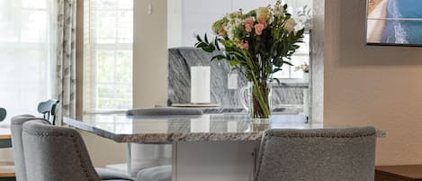 Una cocina moderna con encimera de mármol, dos sillas tapizadas y un florero con flores.