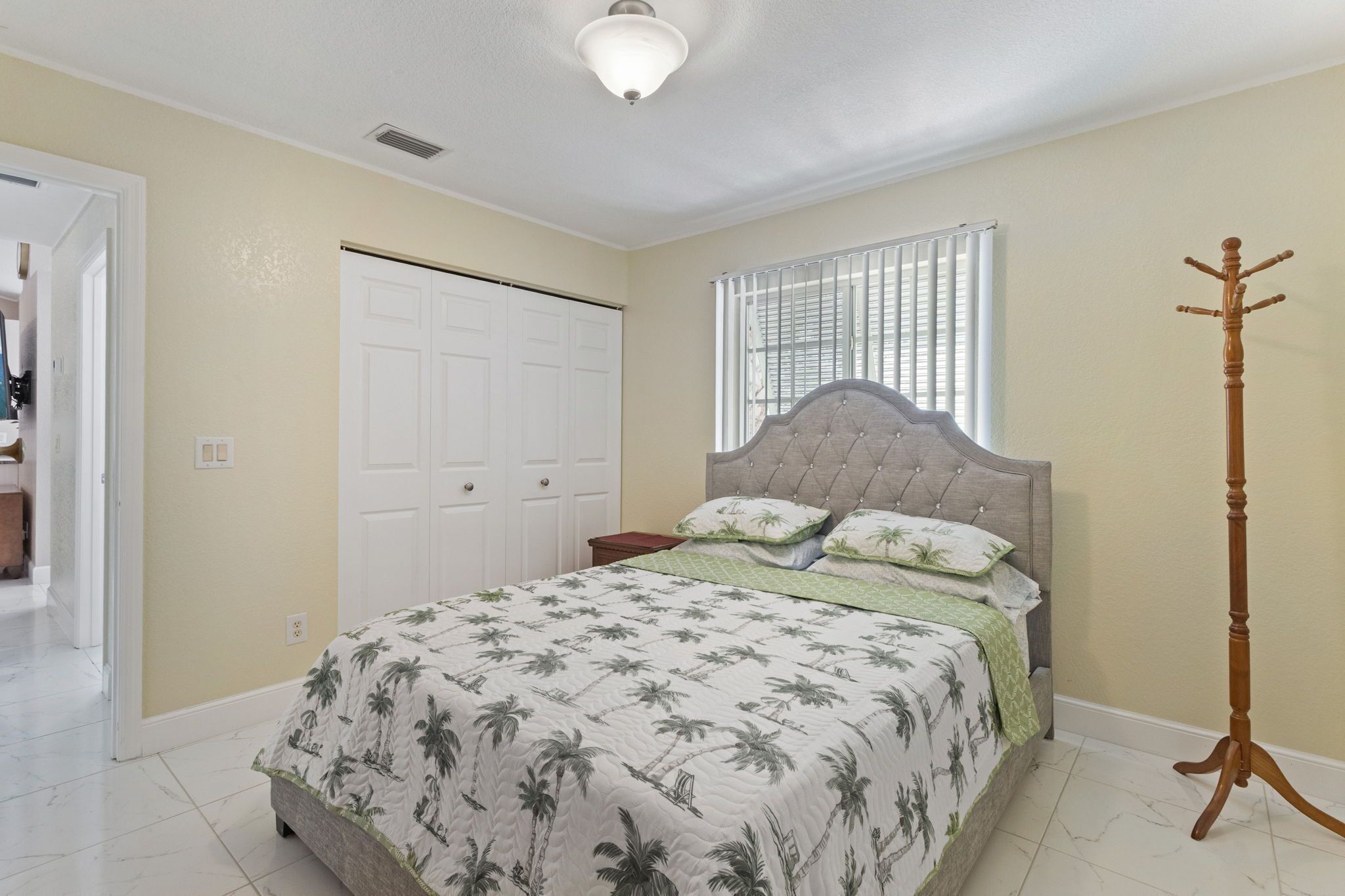 Une chambre à coucher comprenant un lit, une armoire, une fenêtre avec des stores et un porte-manteau.