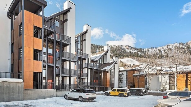 A modern multi-story building with balconies and a parking area. - Fifth Avenue Unit 202 | 2 Bedroom + Loft Condo, Huge Windows & Views. 2 Blocks to Skiing! (Aspen)