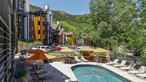 A modern hotel with a pool area, outdoor seating, and a view of the surrounding mountains. - Fifth Avenue Unit 202 | 2 Bedroom + Loft Condo, Huge Windows & Views. 2 Blocks to Skiing! (Aspen)