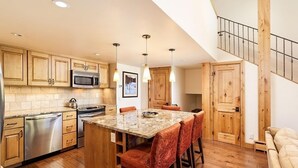 A modern kitchen with wooden cabinets, stainless steel appliances, and a central island with bar stools. - Fifth Avenue Unit 202 | 2 Bedroom + Loft Condo, Huge Windows & Views. 2 Blocks to Skiing! (Aspen)