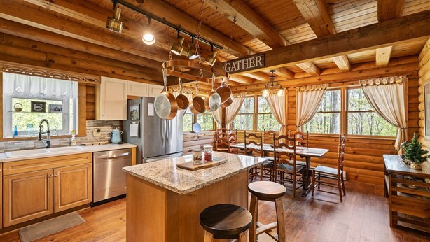 A wooden cabin interior with a kitchen area featuring a central island, bar stools, and a dining table with chairs.
