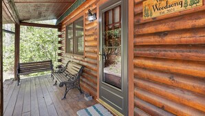 A wooden cabin with a porch, a welcome sign, and a bench.