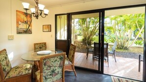Comedor con mesa y sillas de vidrio, una araña y vista a un jardín tropical a través de un gran ventanal corredizo.