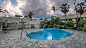 Una piscina con baldosas de piedra, rodeada de palmeras y un edificio con tejado de cerámica.