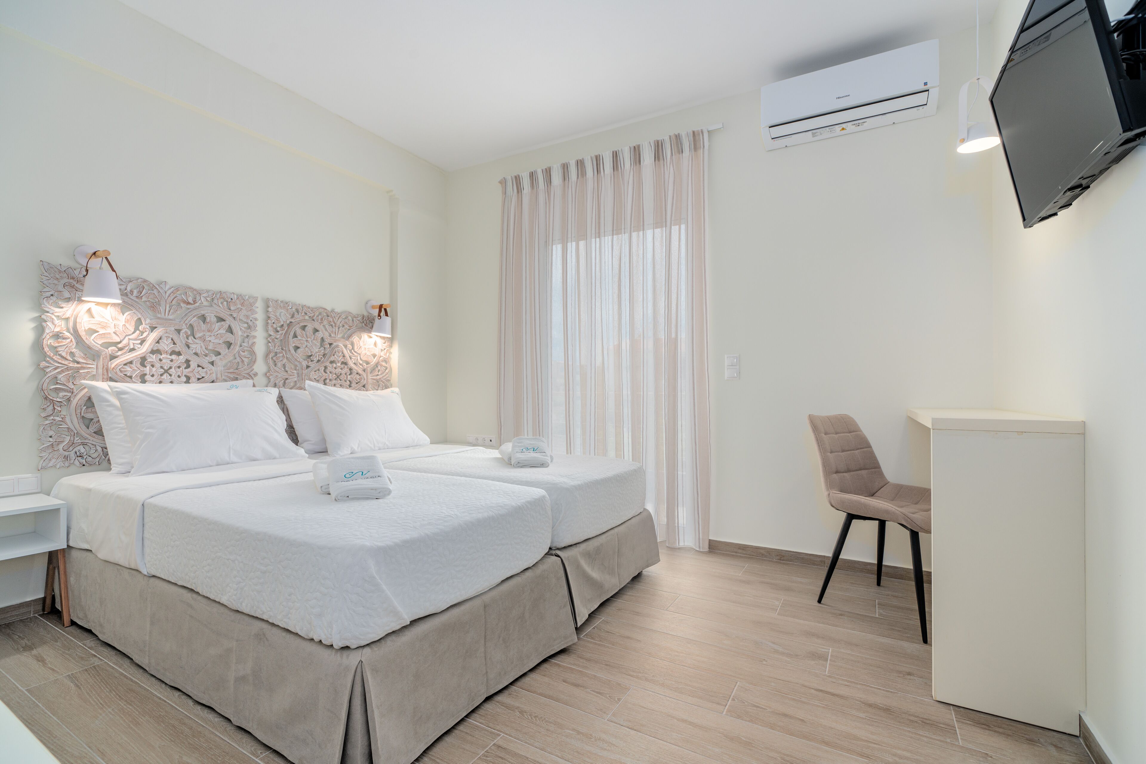 Ein Hotelzimmer mit zwei Betten, einem an der Wand befestigten Fernseher, einem Schreibtisch und einem Stuhl.