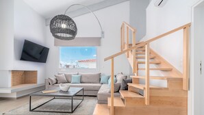 A modern living room with a large window, a wooden staircase, a flat-screen TV, and a cozy seating area. - COSTAVASIA Apartments (Velo-Vocha)