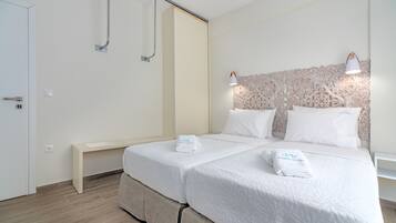 Una habitación de hotel con una cama, dos mesitas de noche, un banco y una lámpara fijada a la pared.