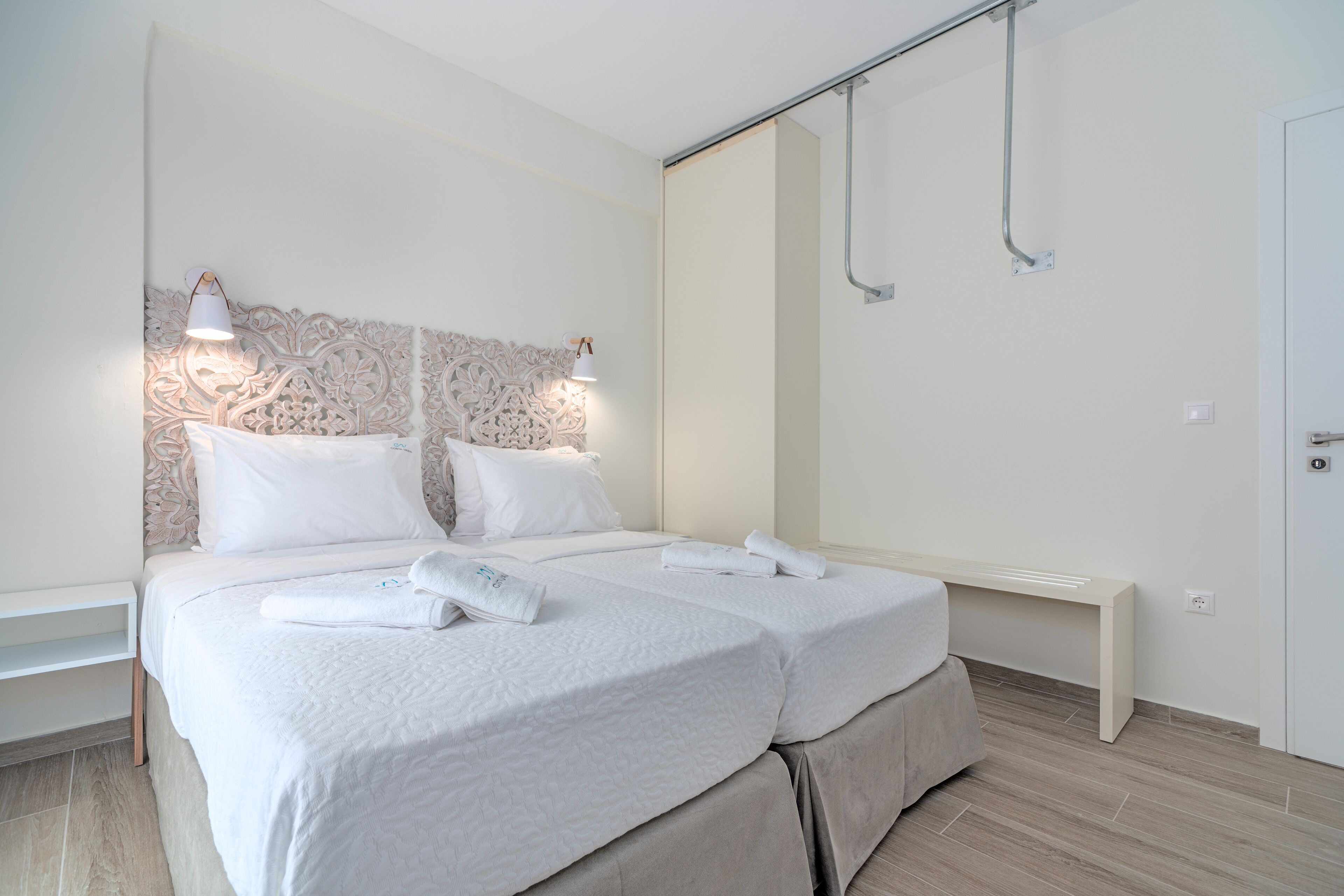 A double bed with white linens, a bedside table, a wall-mounted light fixture, and a shower area.