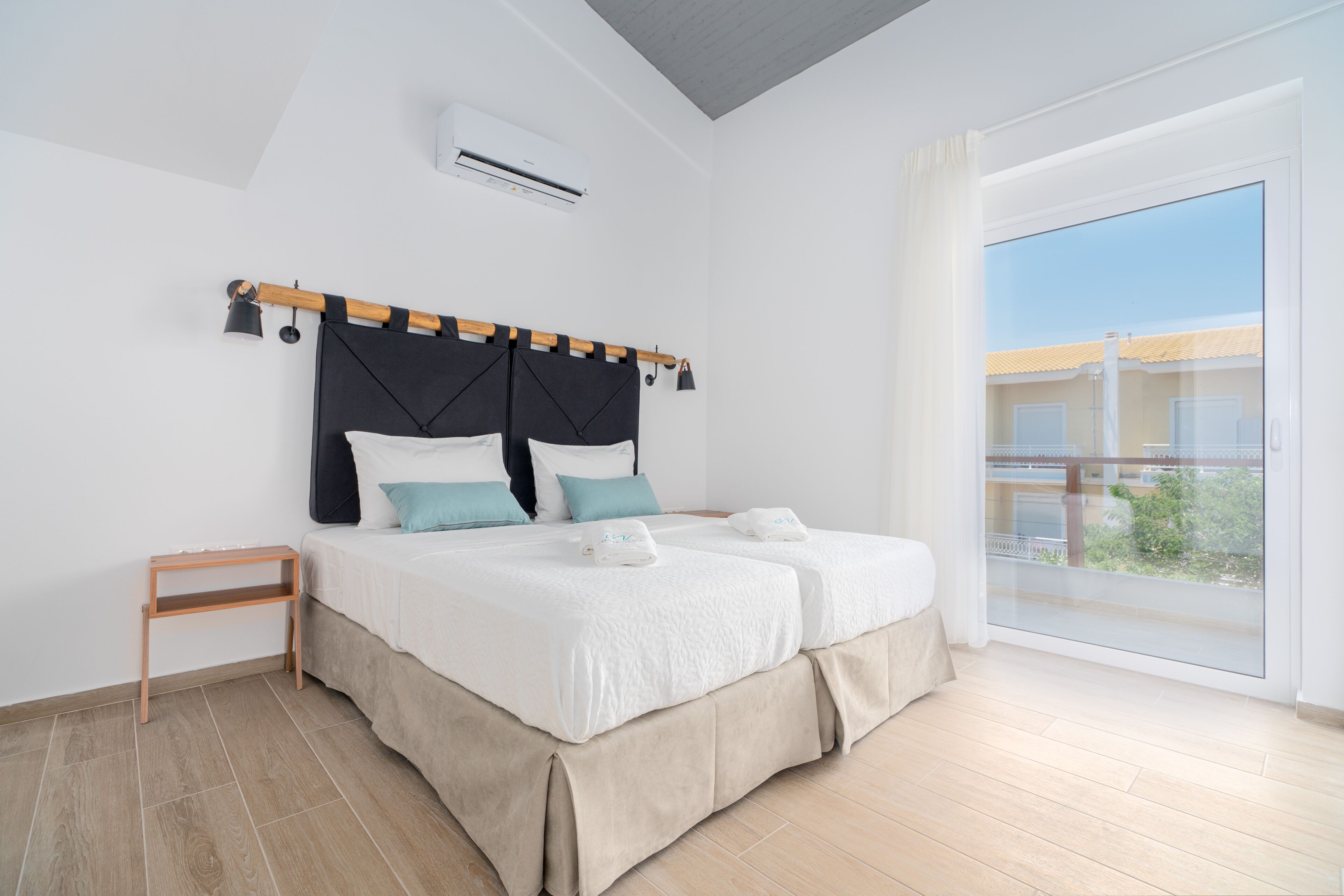 Quarto moderno com cama grande, mesa de cabeceira pequena e janela ampla com vista para edifícios.