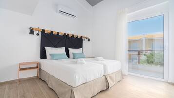 Quarto moderno com cama grande, mesa de cabeceira pequena e janela ampla com vista para edifícios.