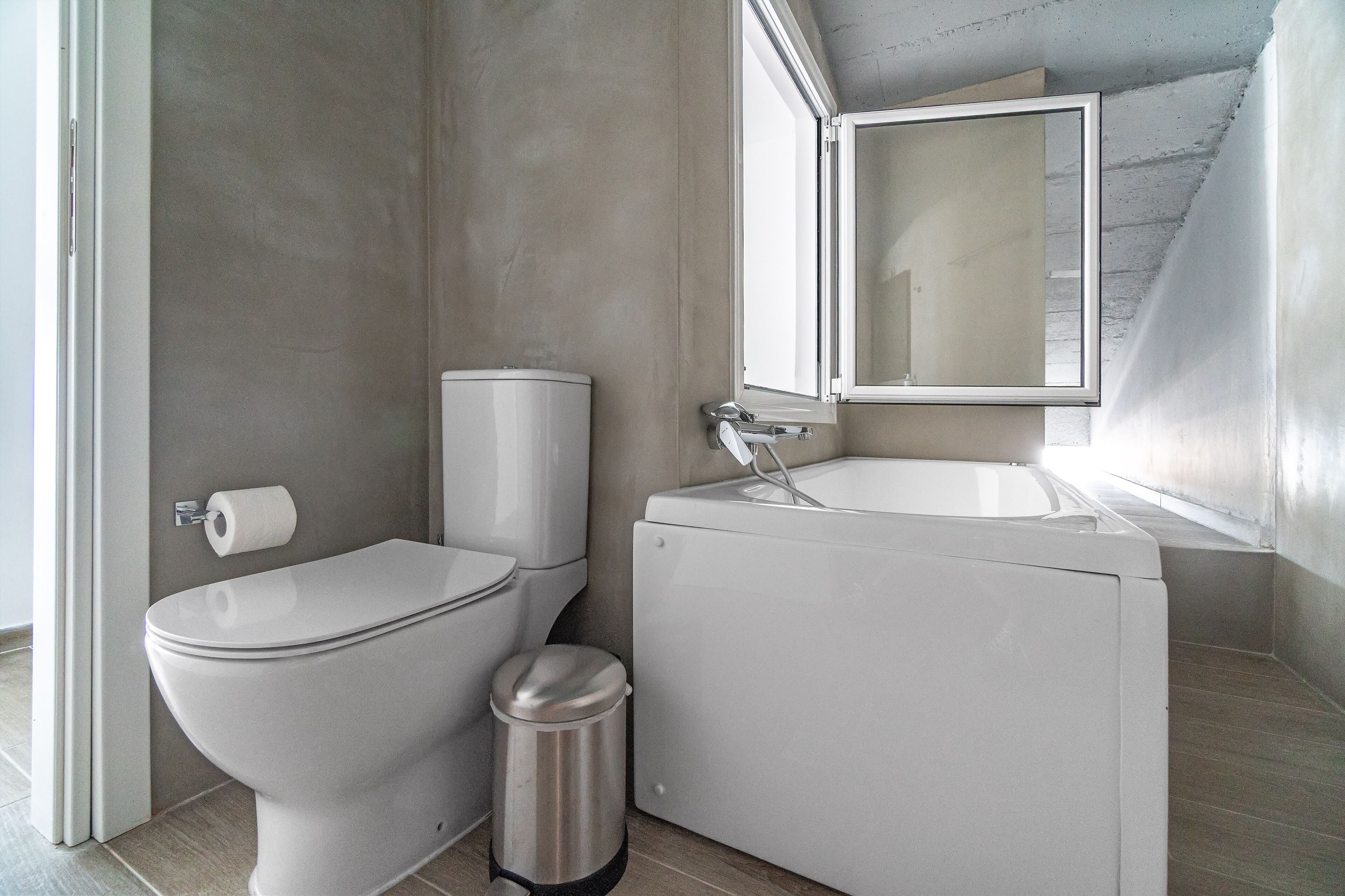 Een badkamer met een toilet, een prullenbak en een wastafel met een spiegel erboven.