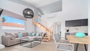 A modern living room with a sofa, coffee table, and a dining area with a table and chairs. There is a staircase leading to an upper level. - COSTAVASIA Apartments (Velo-Vocha)