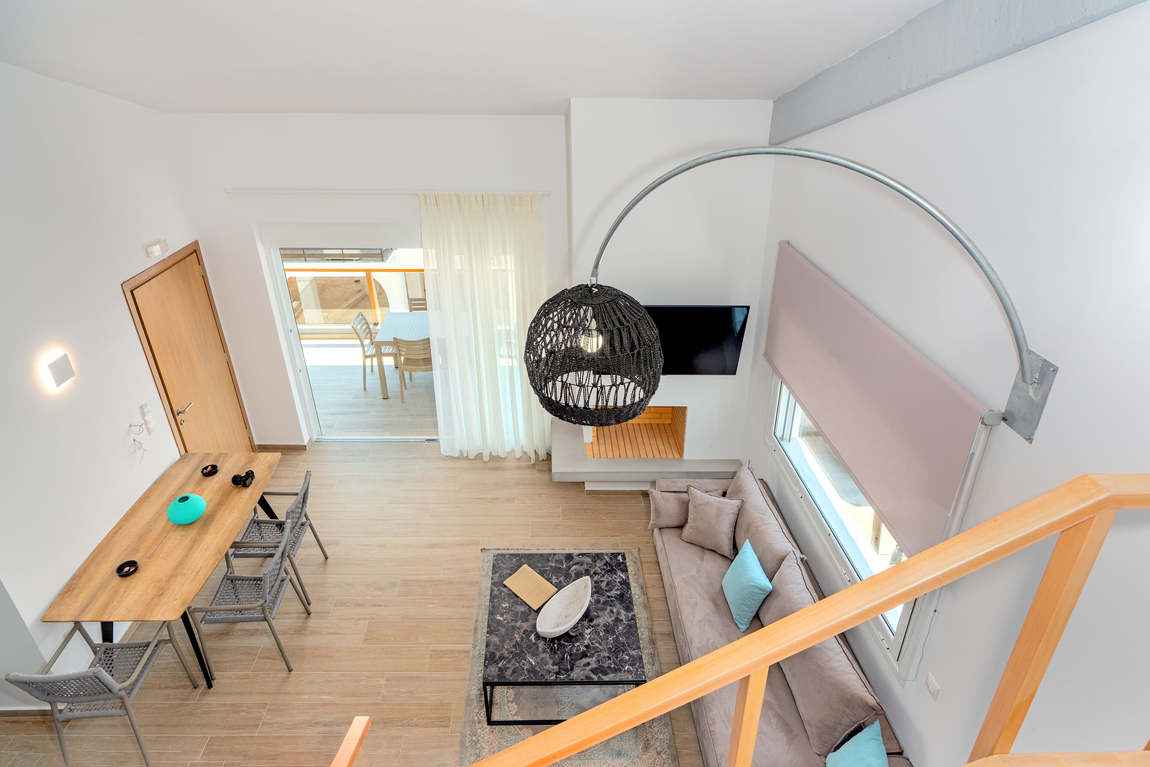 Een moderne woonkamer met een houten eettafel, een bank, een televisie en een trap.
