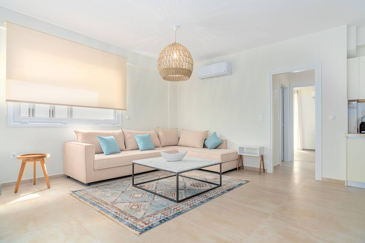 A modern living room with a beige sofa, a glass coffee table, and a woven pendant light.