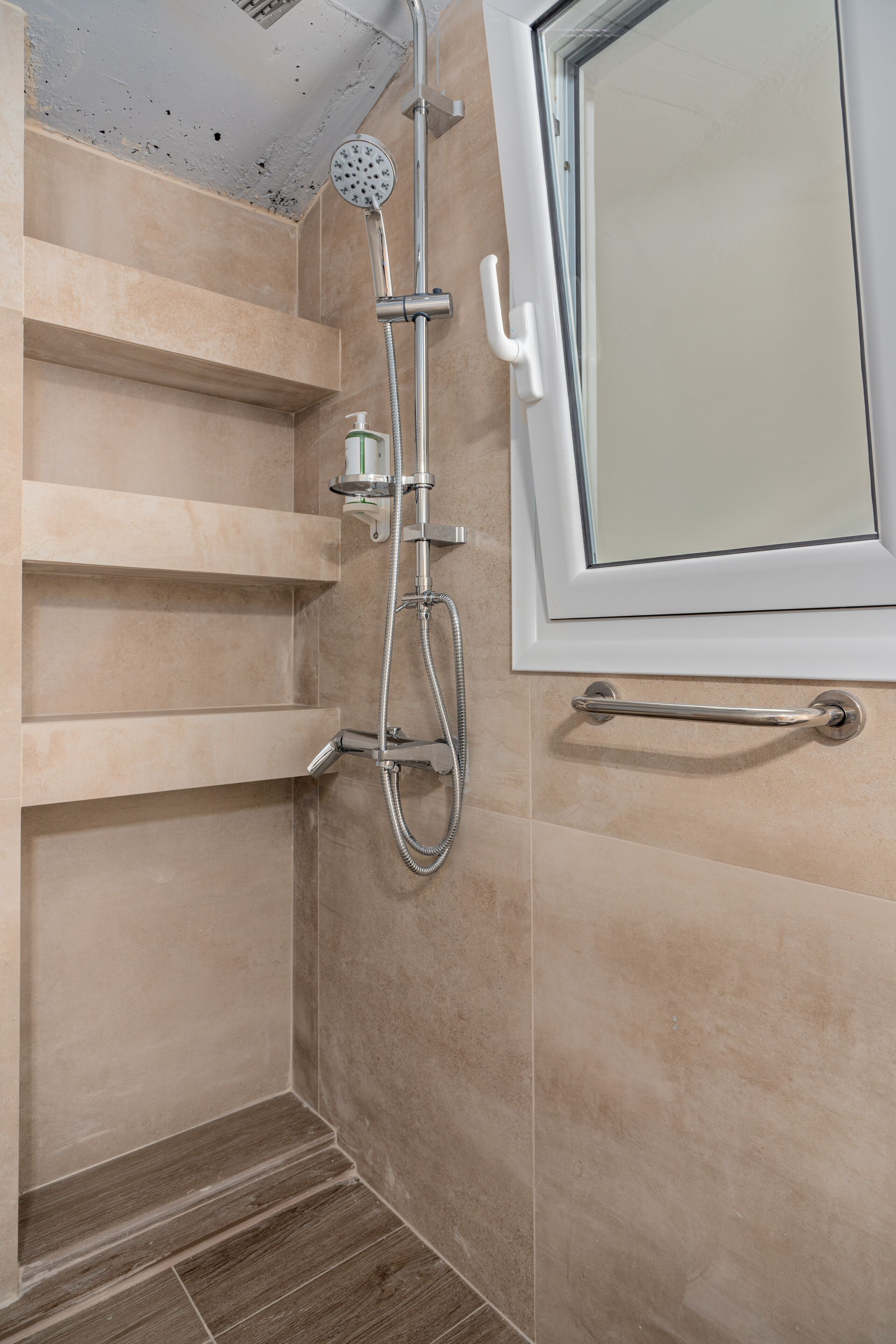 A shower with a handheld showerhead, a wall-mounted faucet, and a glass door with a handle.