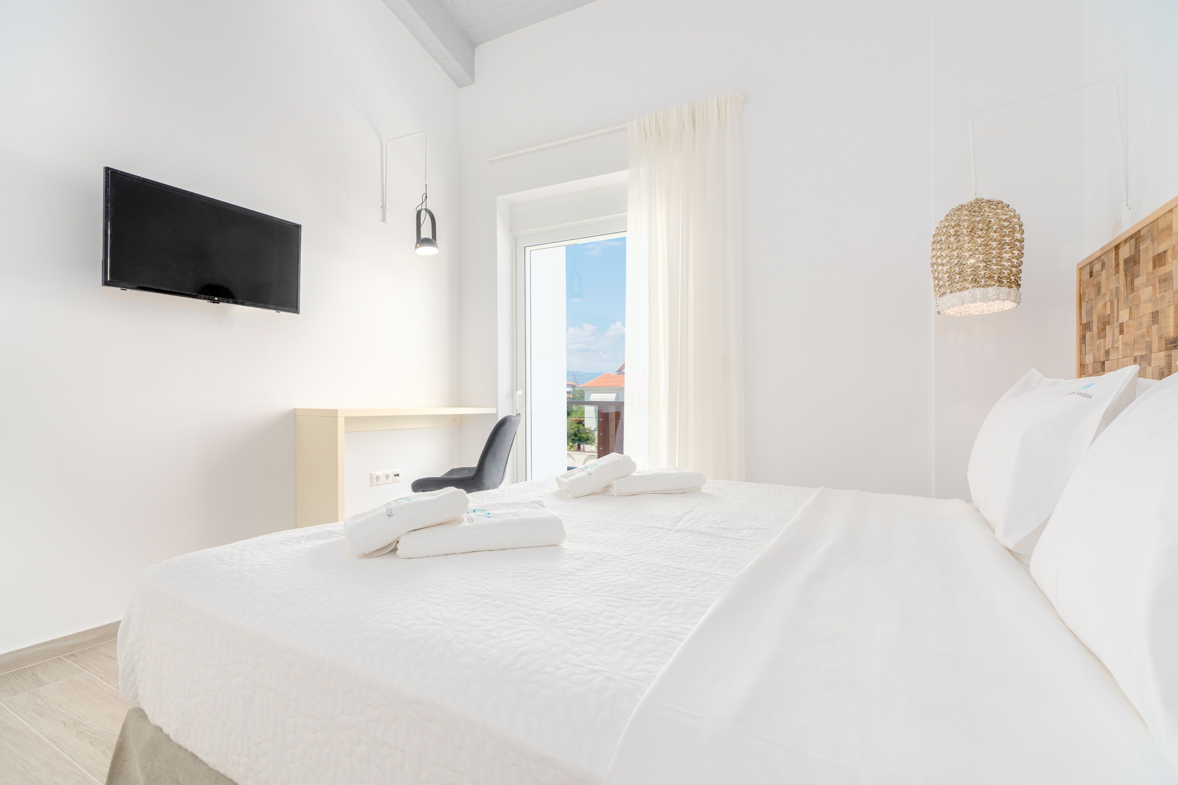 Una habitación de hotel moderna con una cama grande, un televisor de pantalla plana en la pared, un cabecero de madera y vistas al exterior a través de un ventanal amplio.