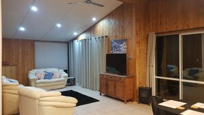 Una sala de estar con un sofá, televisión, un mueble de madera y un ventanal corredero.