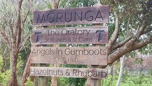 Un letrero de madera con múltiples indicaciones y nombres, incluyendo 'MORUNGA', 'El Oratorio', 'San Francisco y Santa Clara', 'Angels in Gumboots Craft Hub' y 'Avellanas y Ruibarbo'.