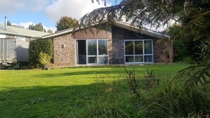 Una casa de dos pisos con fachada de piedra, ventanas amplias y un césped cuidado.