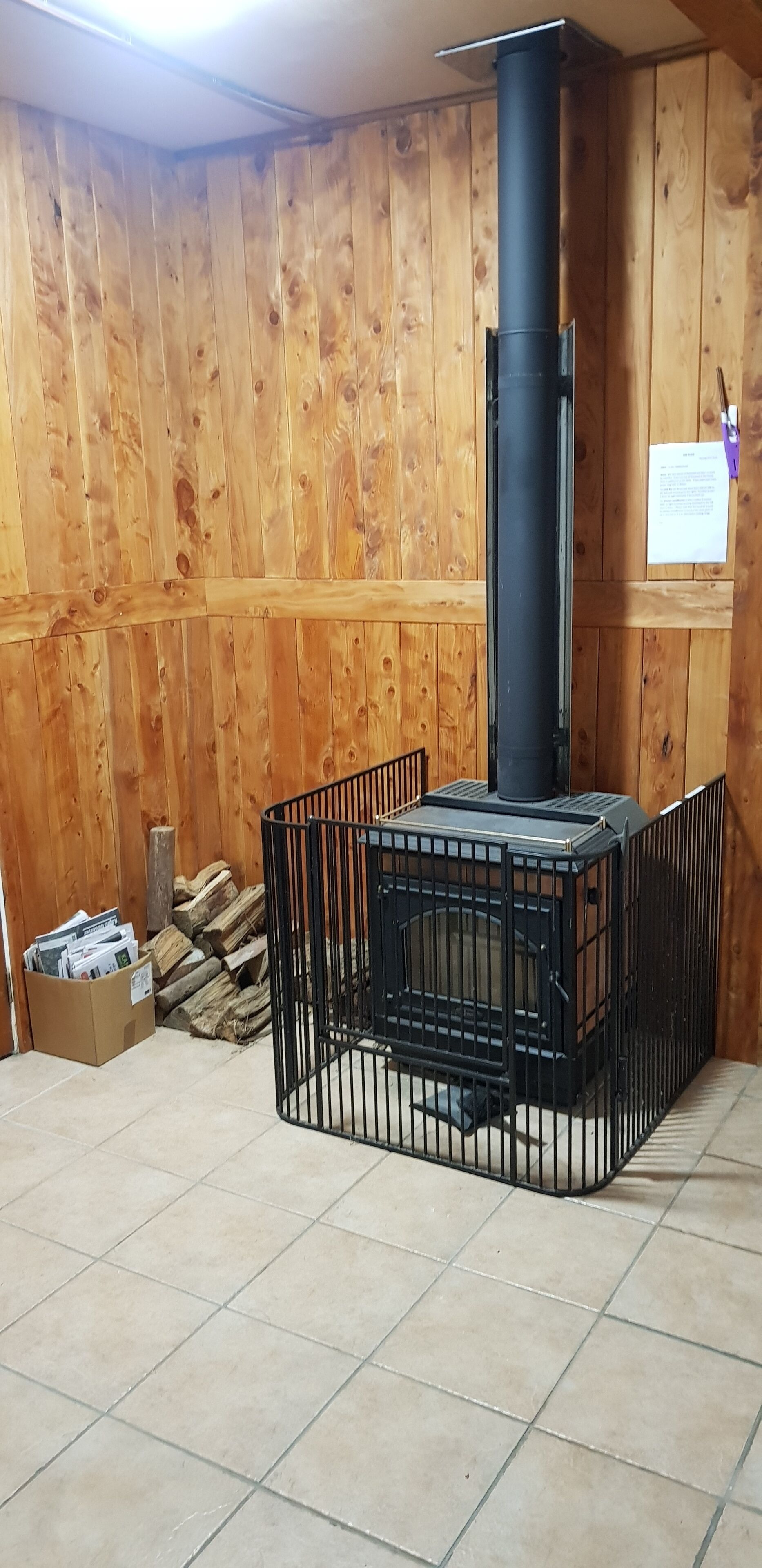 Ett rum med en vedeldad kamin, ett klinkergolv och en väggpanel av trä.