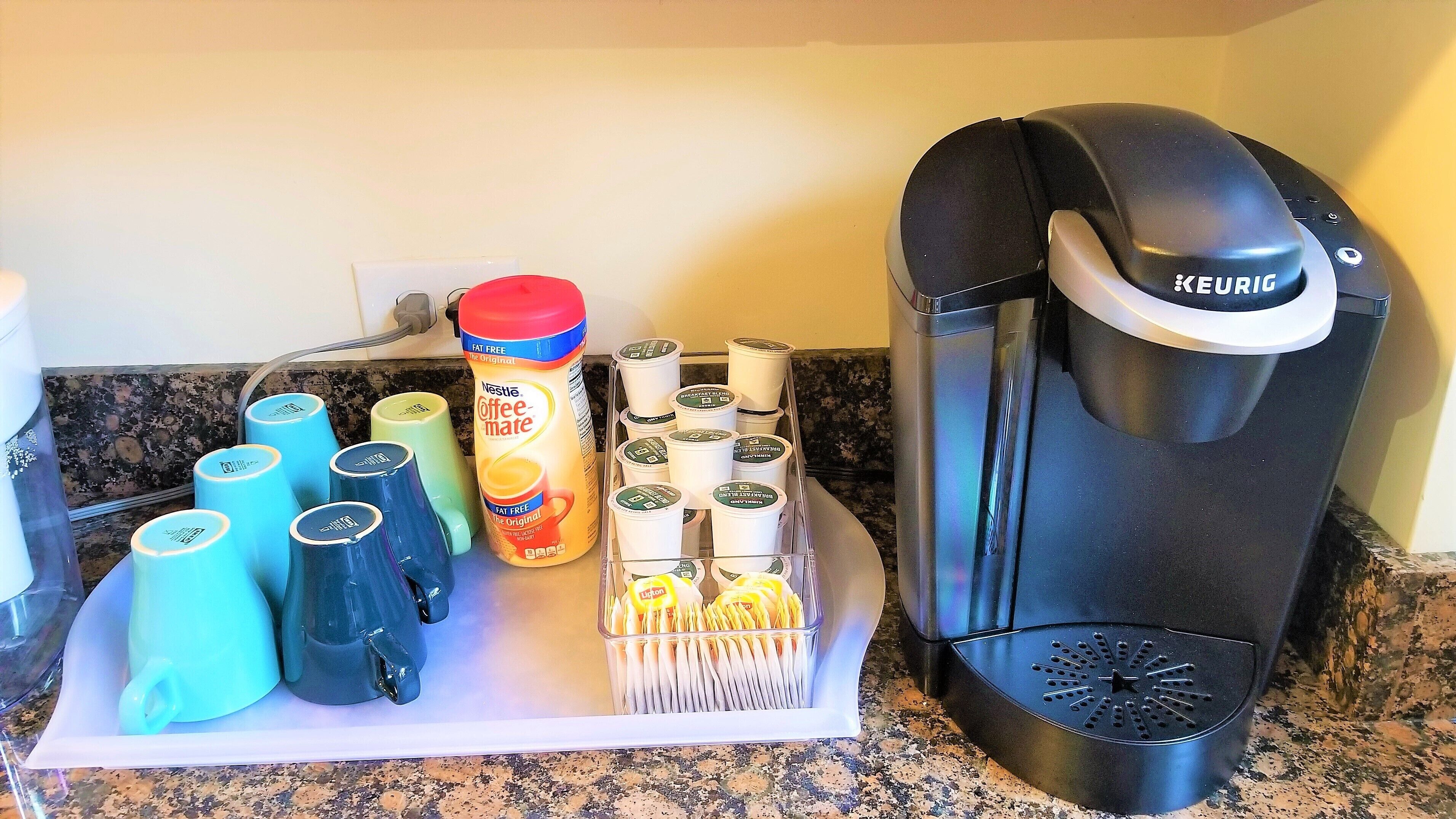 Une machine à café, plusieurs tasses à café et un récipient contenant des dosettes de café, le tout posé sur un plan de travail de cuisine.