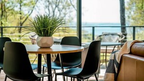 Ein moderner Außenbereich mit Sitzgelegenheit, einem runden Tisch und Stühlen, einem Blumentopf und Blick auf das Meer.