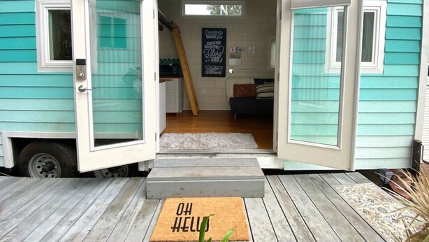 A teal house with a sliding door open, revealing a living area with a sofa, a ladder, and a sign.