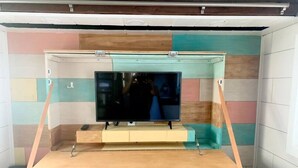 A television mounted on a wooden stand with a colorful, striped wall in the background.