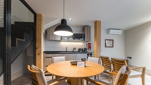 A modern kitchen with wooden cabinets, a black hanging light, and a dining area with a round table and wooden chairs.
