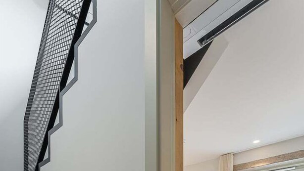 A modern bedroom with a bed, a staircase, and a window with a view of the city.