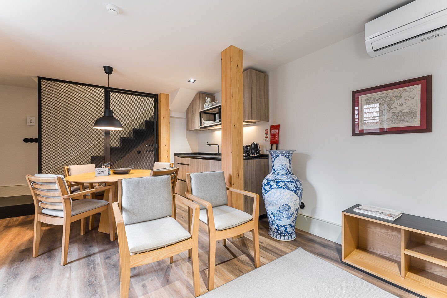 A modern kitchen with wooden cabinets, a dining area with a table and chairs, a large blue vase, and a framed map on the wall.
