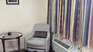 A room with a patterned armchair, a small round table with a remote, and a wall-mounted air conditioner. - Great Western Inn & Suites - Saginaw (Fort Worth)