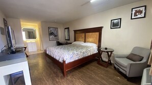 A bedroom with a wooden bed, a desk with a computer, a chair, and a small table. - Great Western Inn & Suites - Saginaw (Fort Worth)