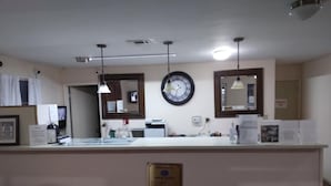 A reception area with a white counter, a clock, and two pendant lights. - Great Western Inn & Suites - Saginaw (Fort Worth)