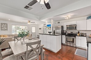 A modern kitchen with white cabinets, stainless steel appliances, and a dining area with a wooden table and chairs. - MODERN LIVING! CAMELBACK EAST-BILTMORE HOME (Phoenix)