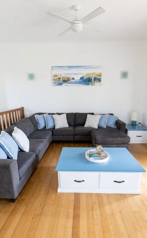 A modern living room with a sectional sofa, a blue coffee table, and a ceiling fan. - Hamilton Island 3BR Ocean View Apartment + Buggy & Transfers | Family Friendly (Whitsundays)