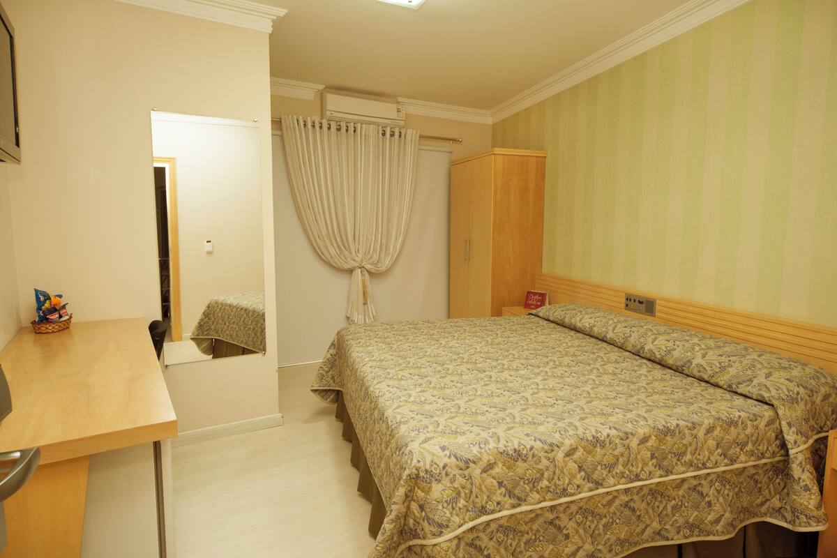 Un dormitorio con cama, escritorio, silla, armario y cortina.