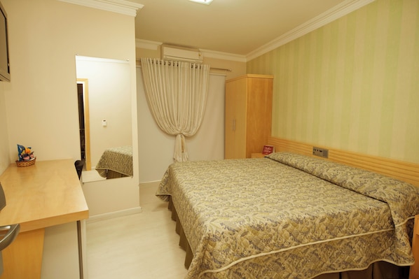 A bedroom with a bed, a desk, a chair, a wardrobe, and a curtain.