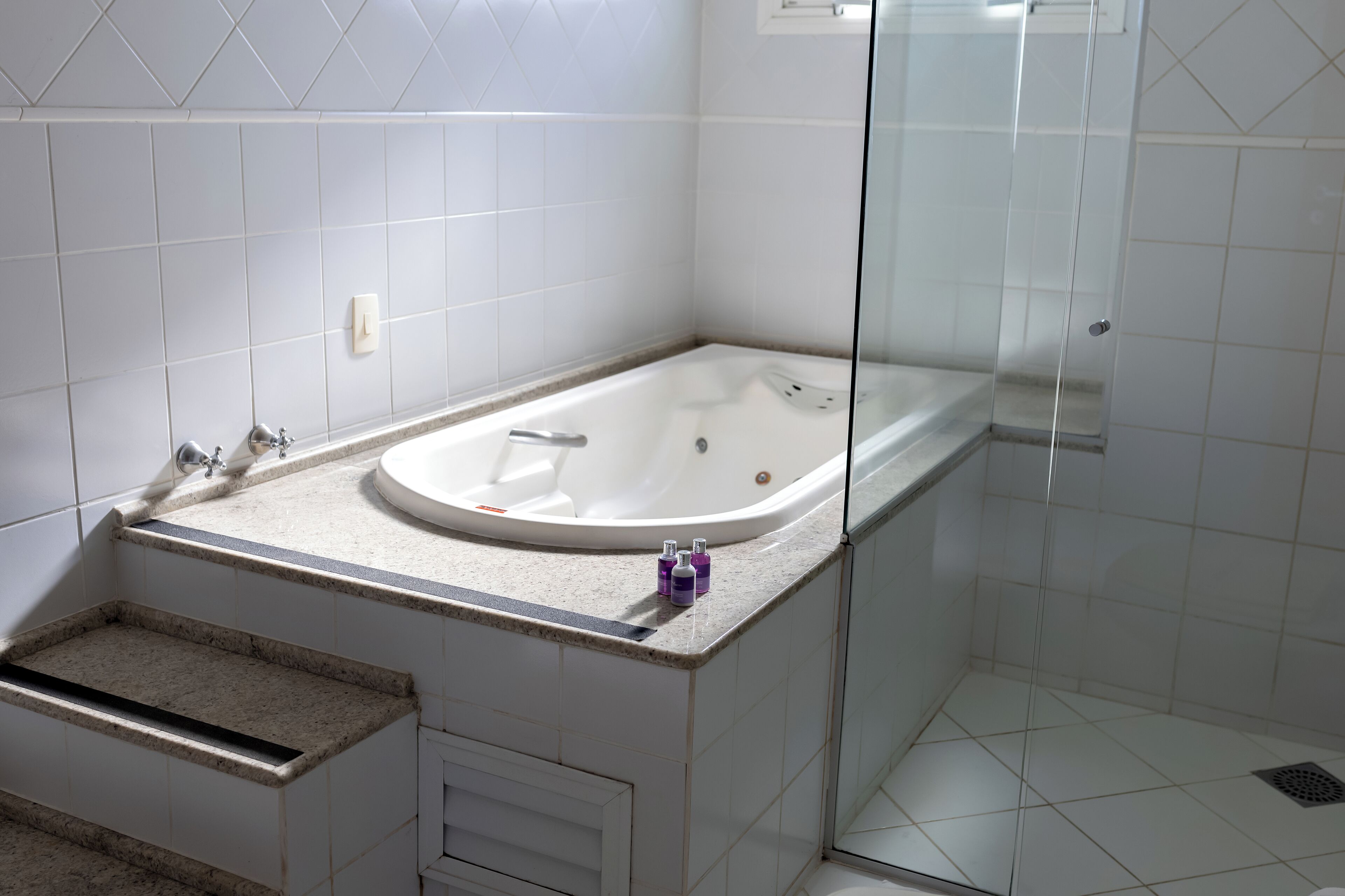 A modern bathroom with a freestanding bathtub, a glass-enclosed shower, and a small step leading to a vanity area.