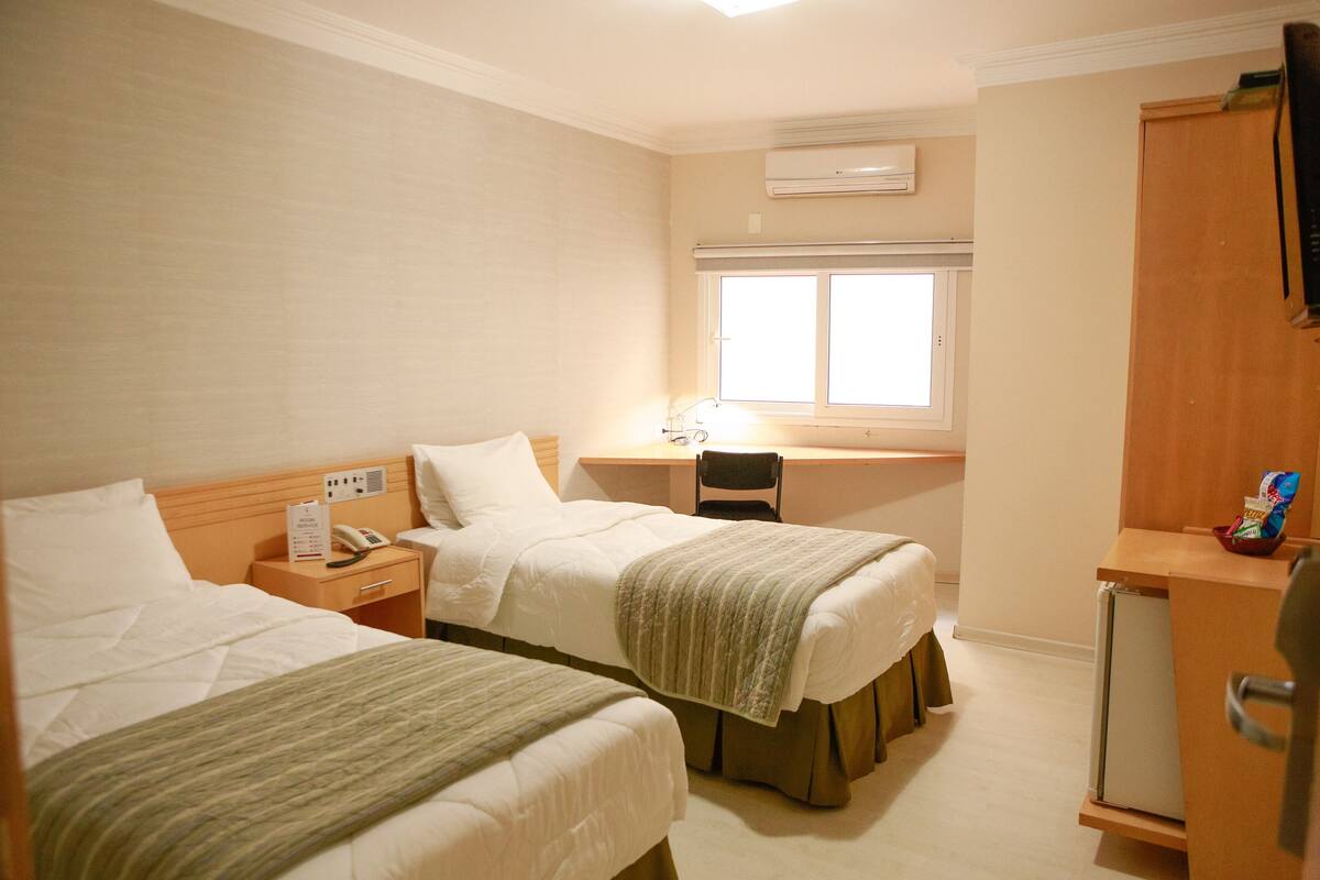 Una habitación de hotel con dos camas, un escritorio, una silla, un refrigerador pequeño y un equipo de aire acondicionado.