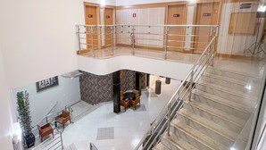 A multi-level hotel lobby with a central seating area, a staircase, and a mezzanine level with lockers. - GoldMen Select Cianorte (Cianorte)