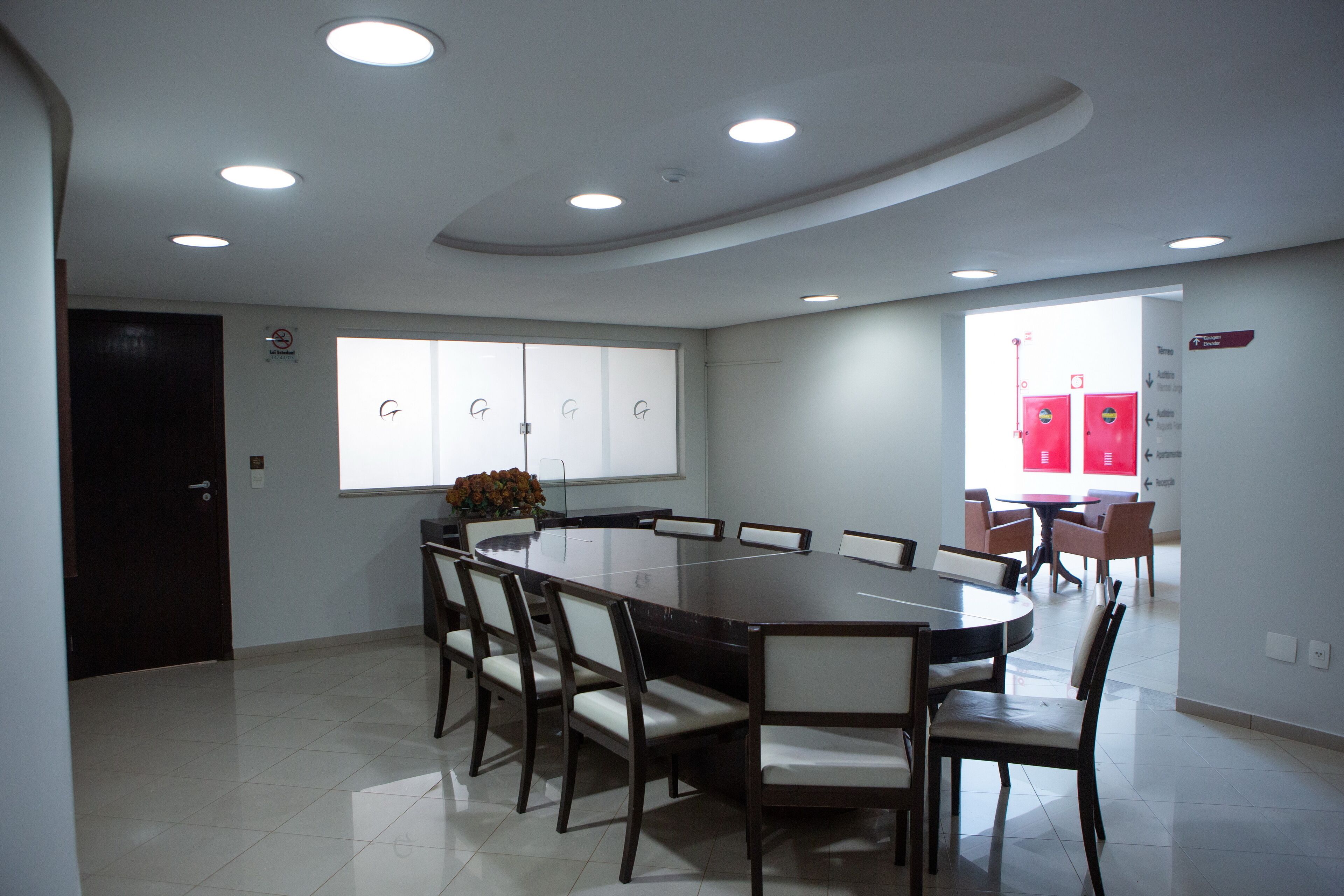 A modern dining area with a large round table surrounded by chairs, recessed ceiling lights, and a view of a red door in the background.