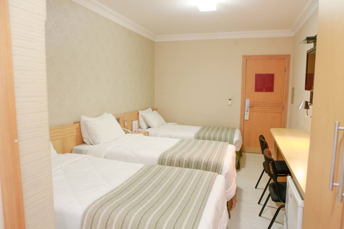 Habitación de hotel con dos camas individuales, un escritorio pequeño, una silla y una puerta con un aviso rojo.