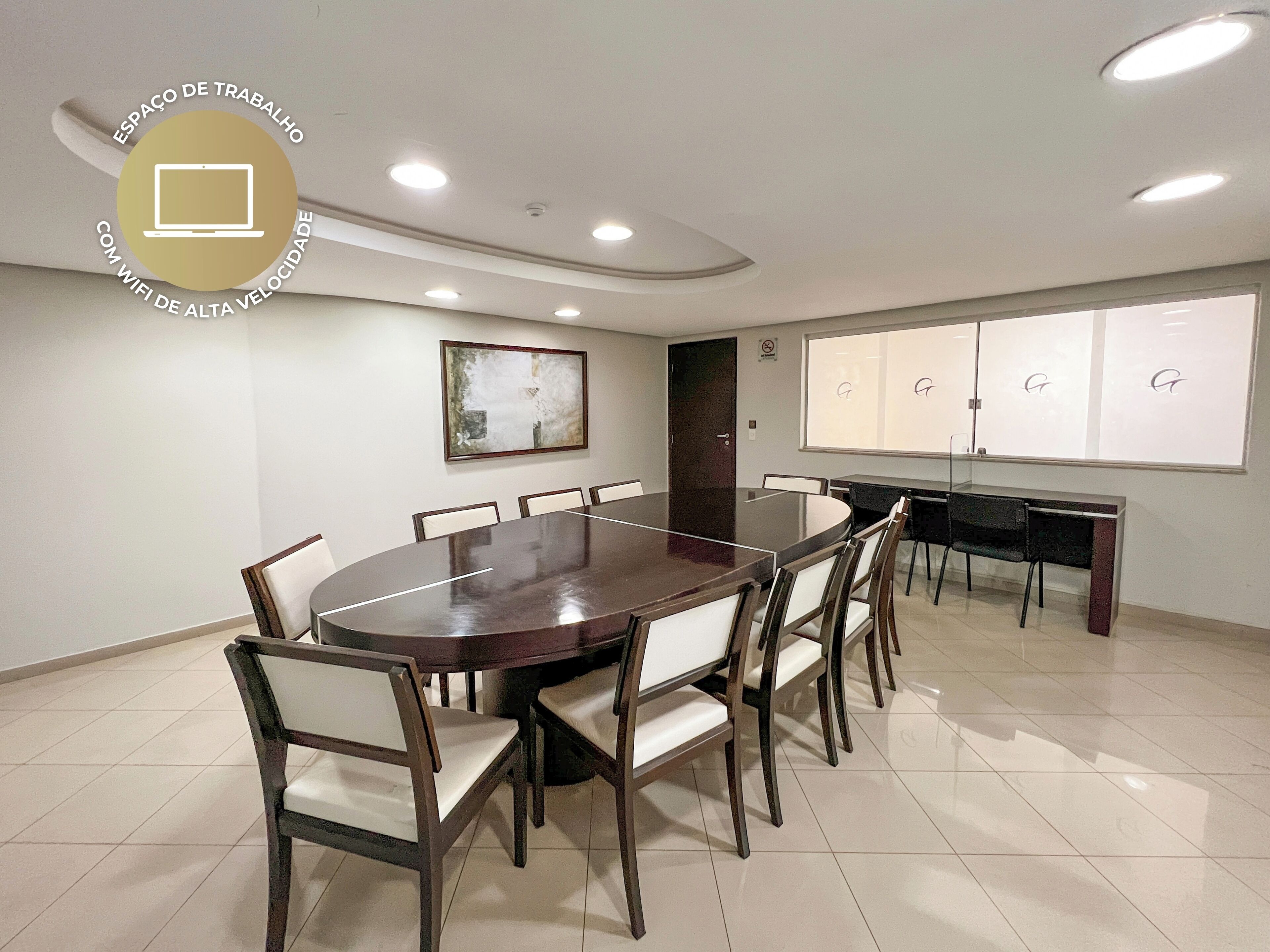A conference room with a large oval table, white chairs, a black desk, and a whiteboard with letters.