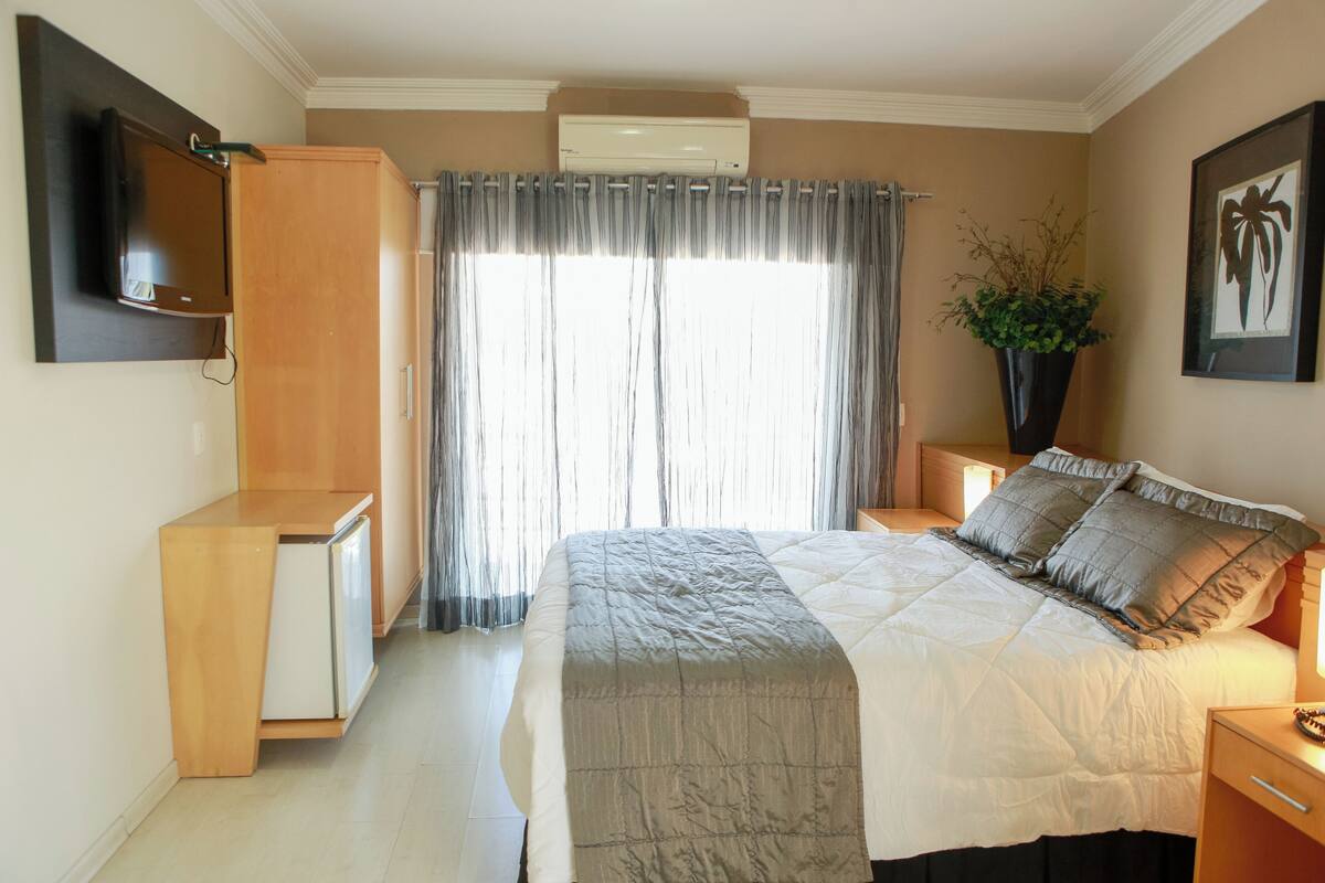 Un dormitorio con una cama, televisión, escritorio y una planta.