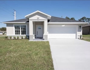 Simple, single-story home with a flat roof, front porch, and garage, set amidst a well-maintained lawn.