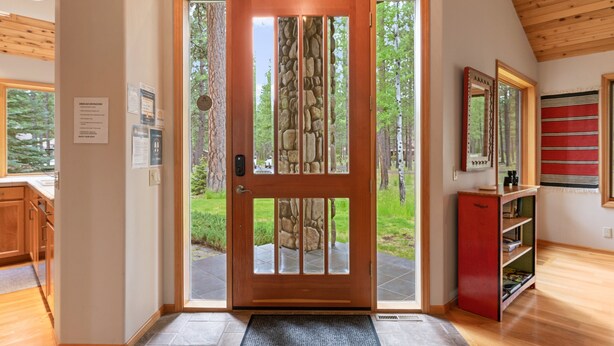 Uma porta de madeira com detalhes em pedra, um armário vermelho e vista para uma área arborizada.